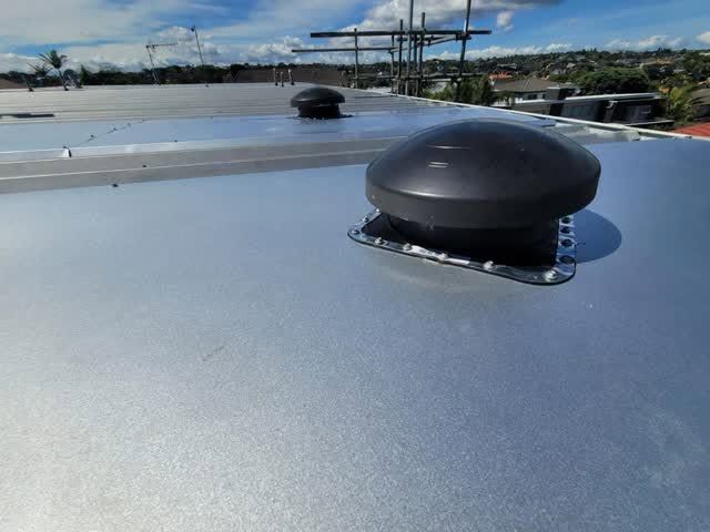 Grey membrane roof finished around a dark roof vent, with suburbs beyond